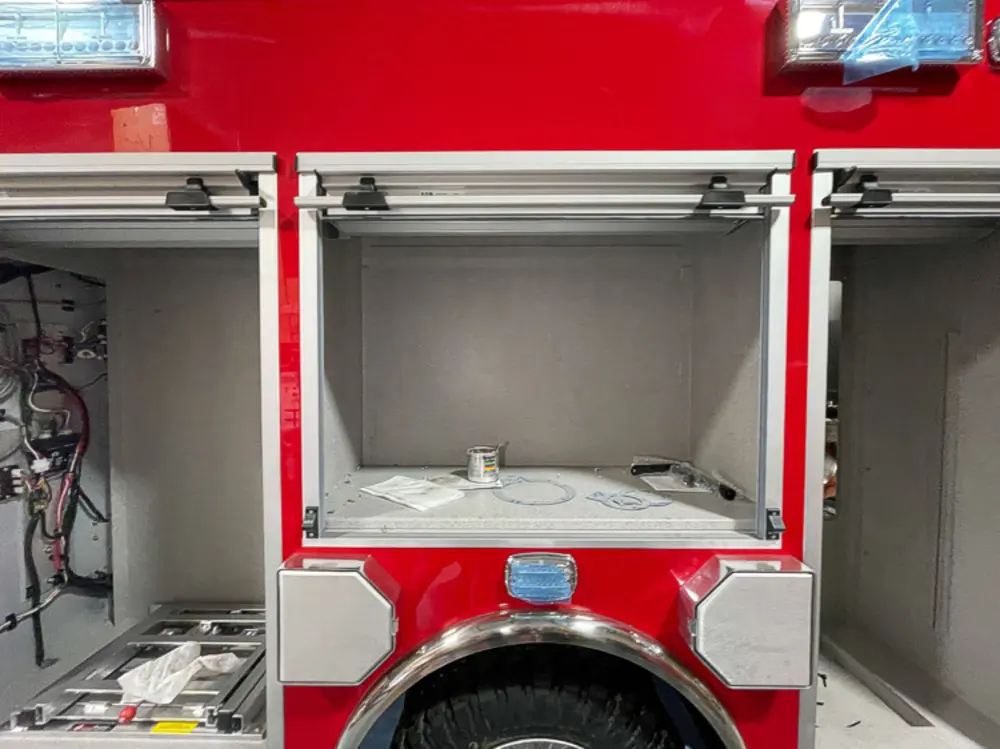 Exterior view of small fire truck showing cab, body compartments, and wheel/tire area.